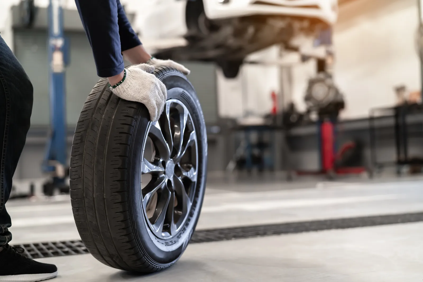 Mechanic rolling a brand new tire to a lifted car