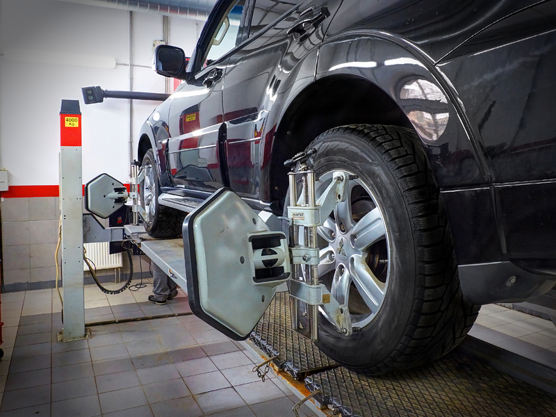 Black car on a mechanical ramp, with a mechanic doing a full service on the car